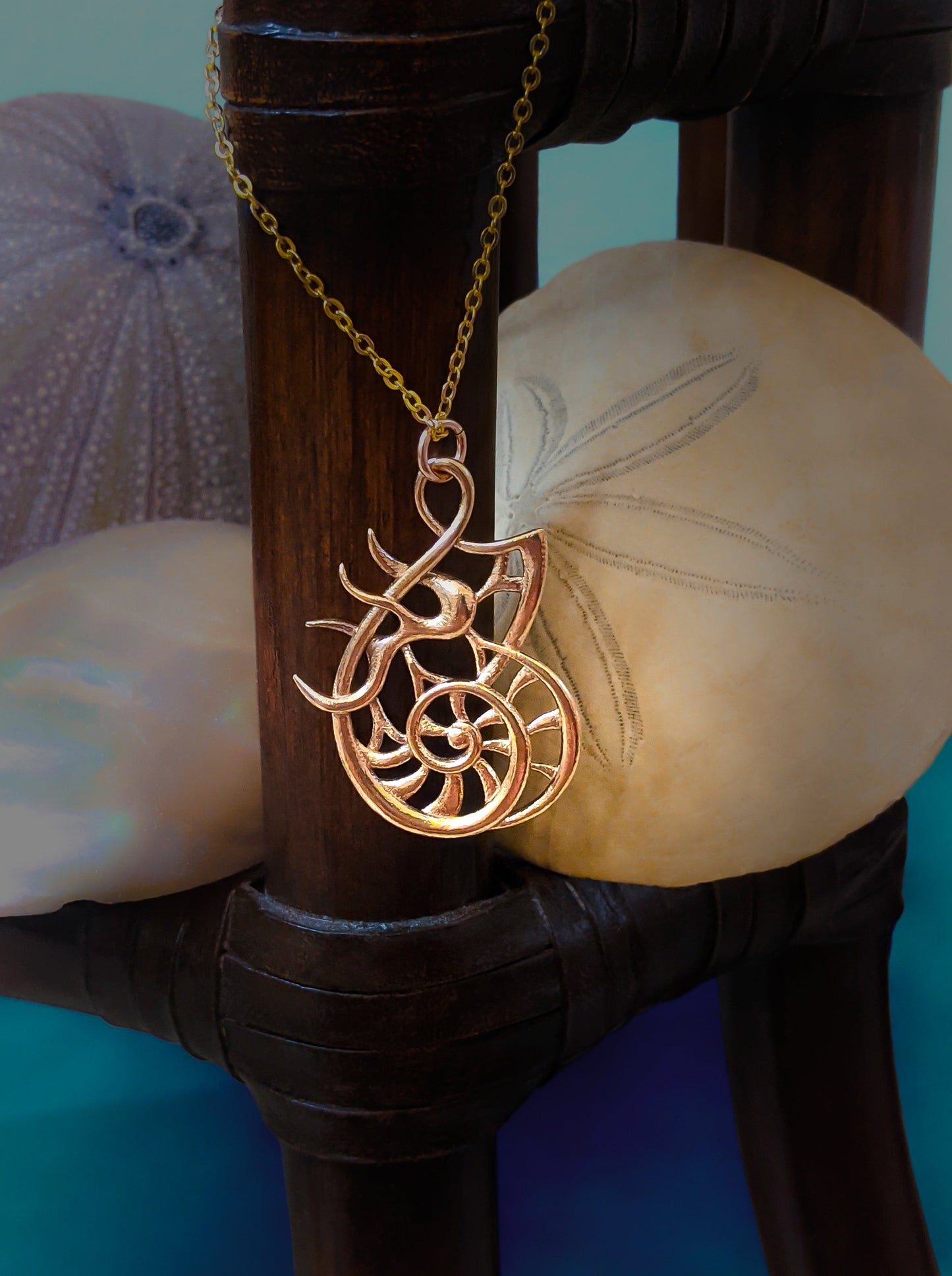 The Sea Chariot pendant hangs around a wood column with assorted shells behind it.