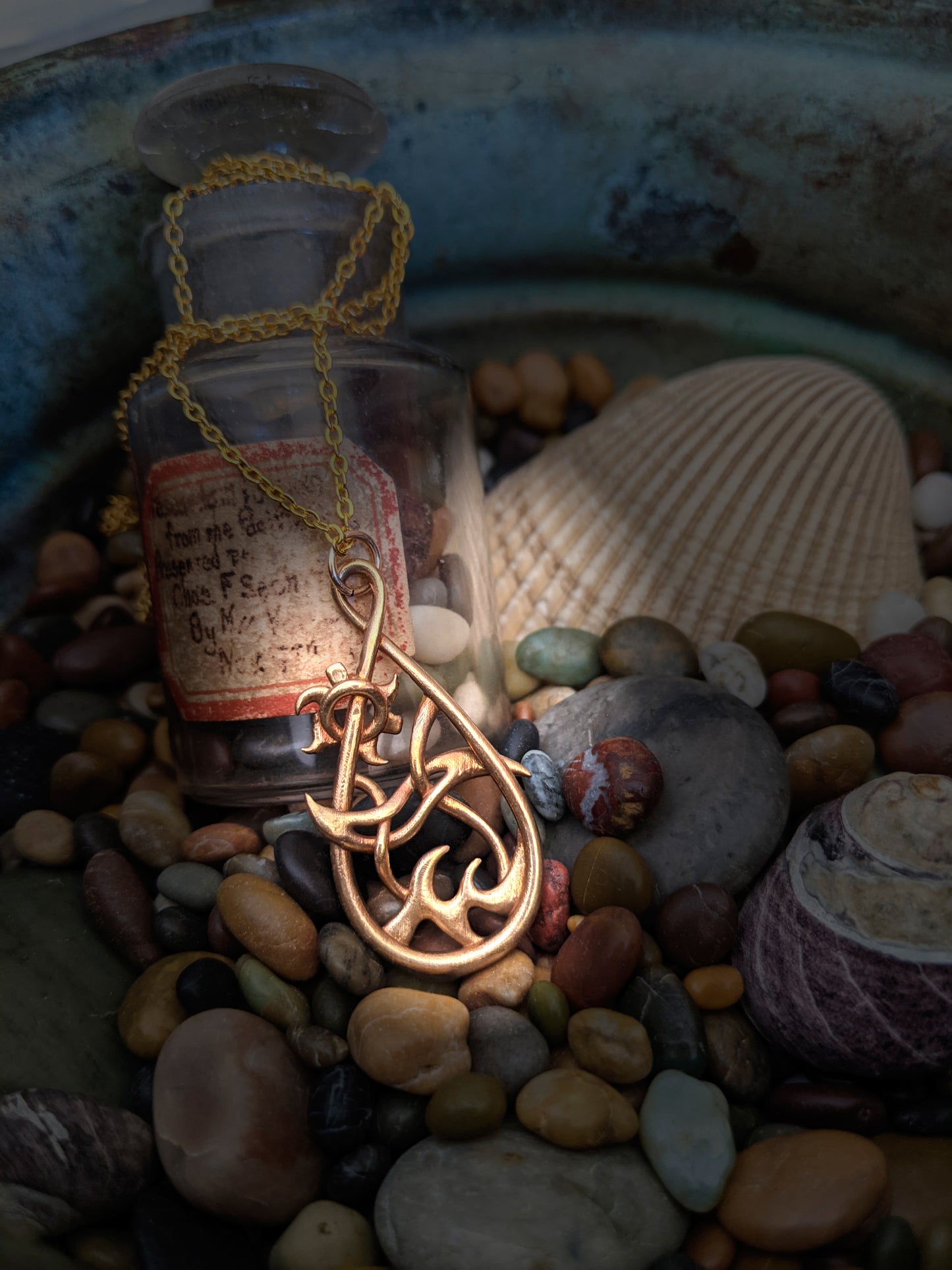 The bronze Seaside pendant rests against a small bottle of pebbles, colorful rocks and shells.