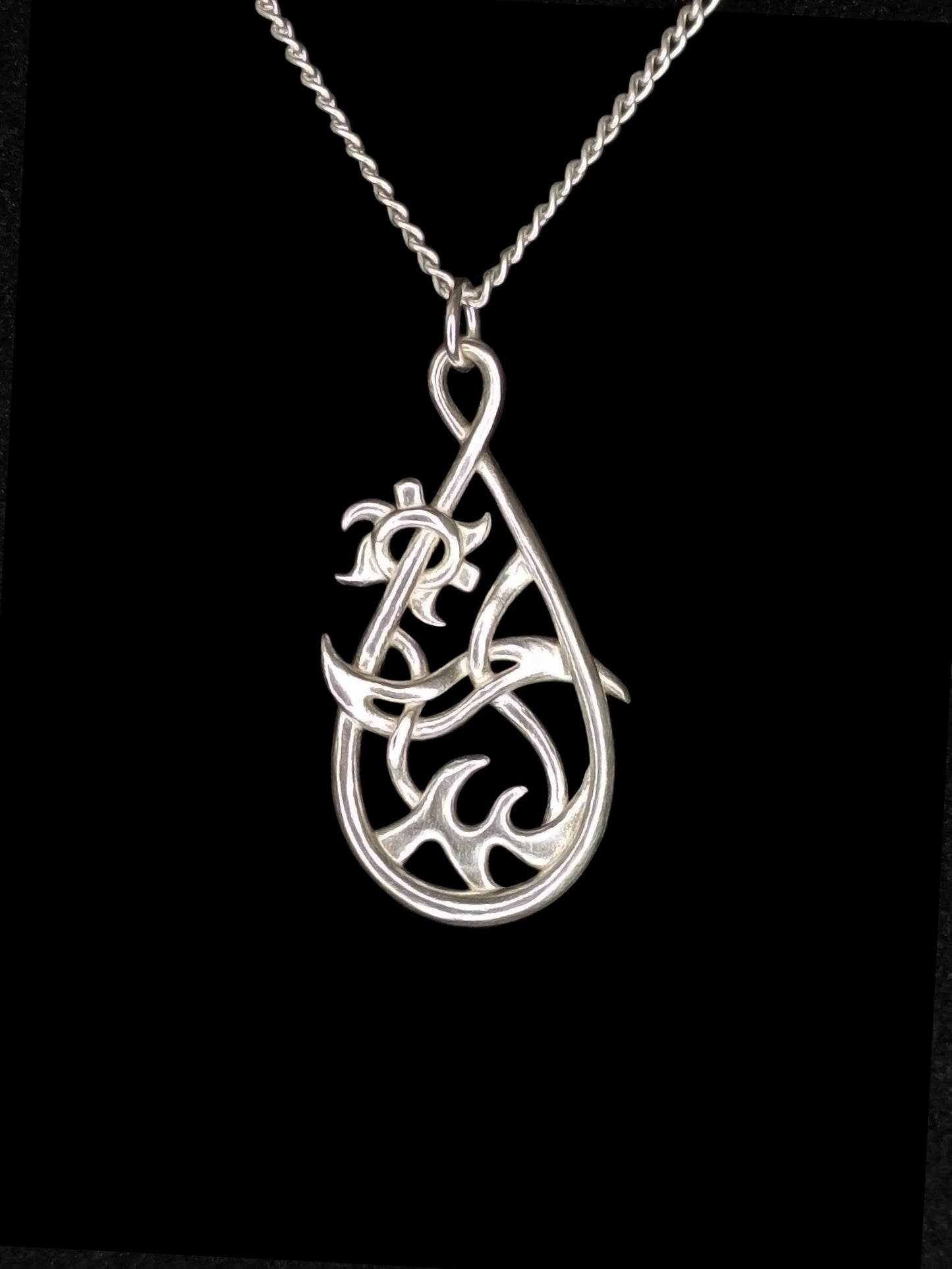 Silver teardrop pendant with waves at bottom, a reversed tilde in the center, and a gear-like sun on the upper left.