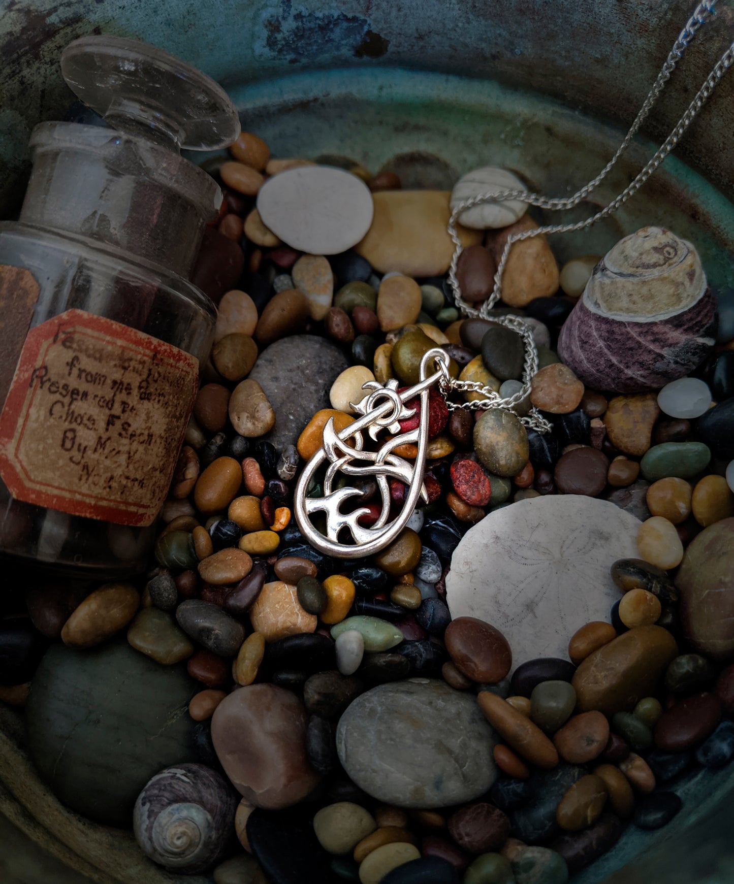 Silver Seaside pendant resting against colorful rocks and shells.