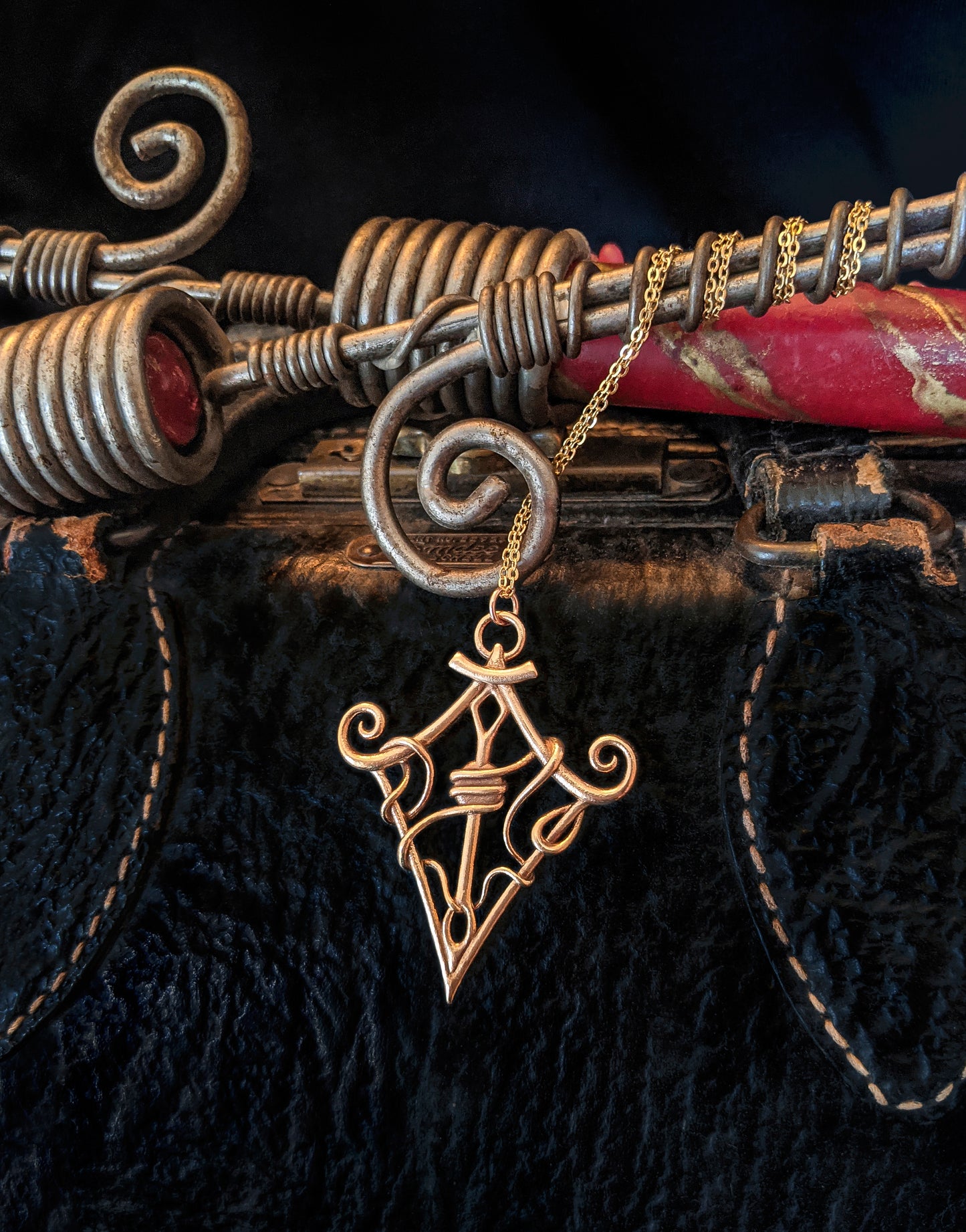 "Through the Eye" bronze pendant against black textured leather, hanging from twisted candlestick holders.