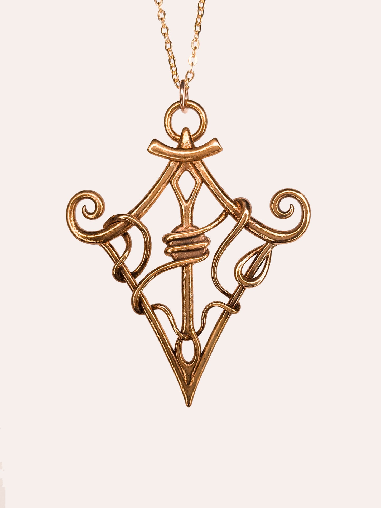 Bronze pendant of a quadrilateral with spirals. A needle pierces through the center. Thread winds all around the shape and through the needle.